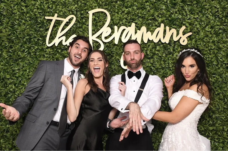 Wedding party striking playful poses in front of a green photo booth backdrop